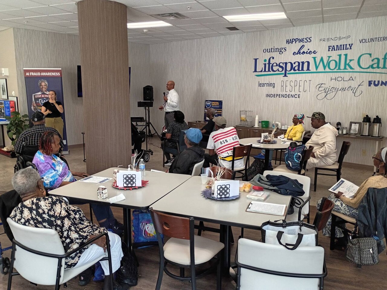 An American Sign Language interpreter signs alongside the presenter during the StopAiFraud AI fraud awareness presentation at Lifespan Walk Café, making the session accessible to all attendees.