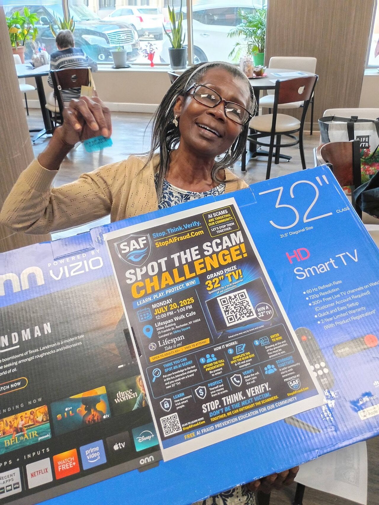 A community member smiles while holding her raffle-prize television at the StopAiFraud AI fraud awareness event at Lifespan Walk Café.